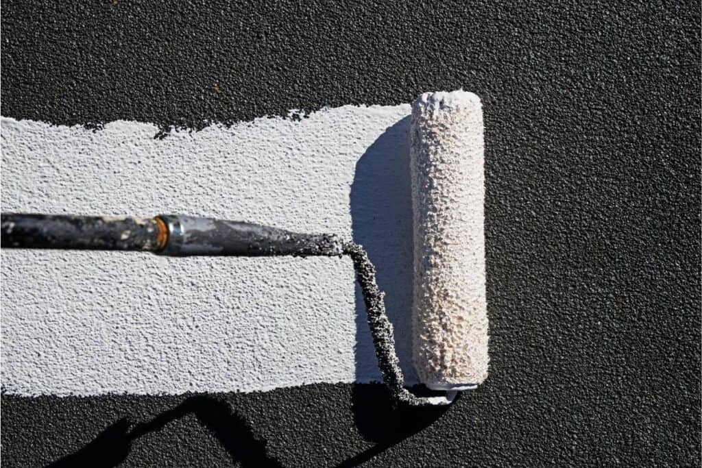 Close-up of a paint roller applying white paint on an asphalt surface, creating a stark contrast.
